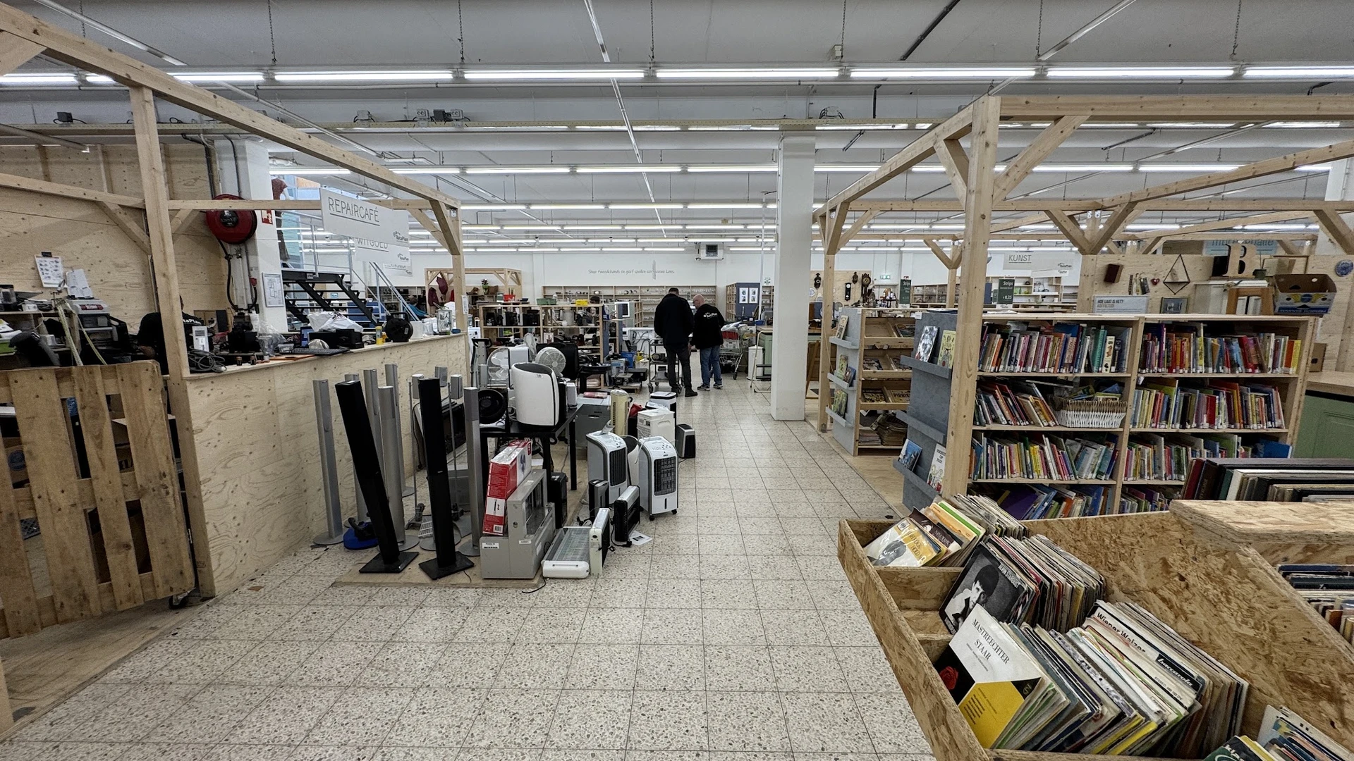Winkelvloer met houten stellingen vol boeken, vinyl en andere tweedehandsartikelen, heldere verlichting van boven