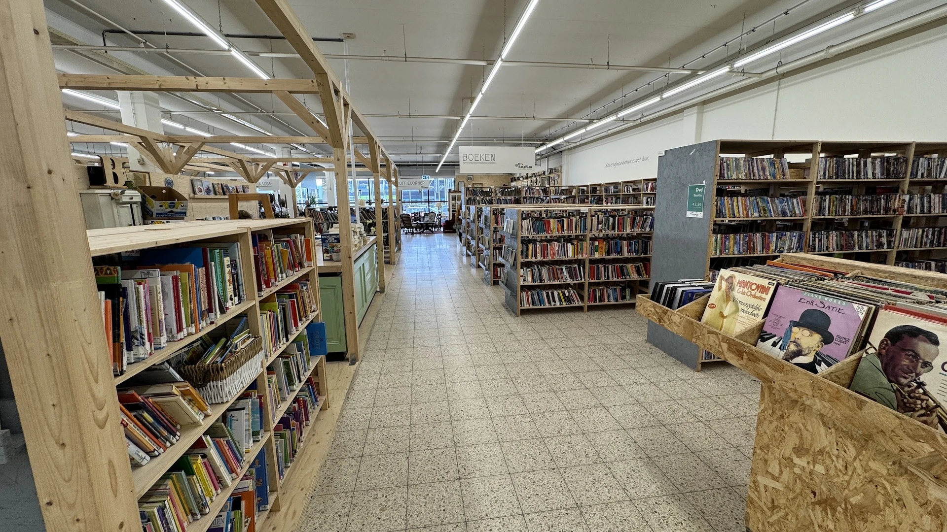 Binnenzicht van kringloopwinkel met boekenrekken, houten steunbalken en leesplekken