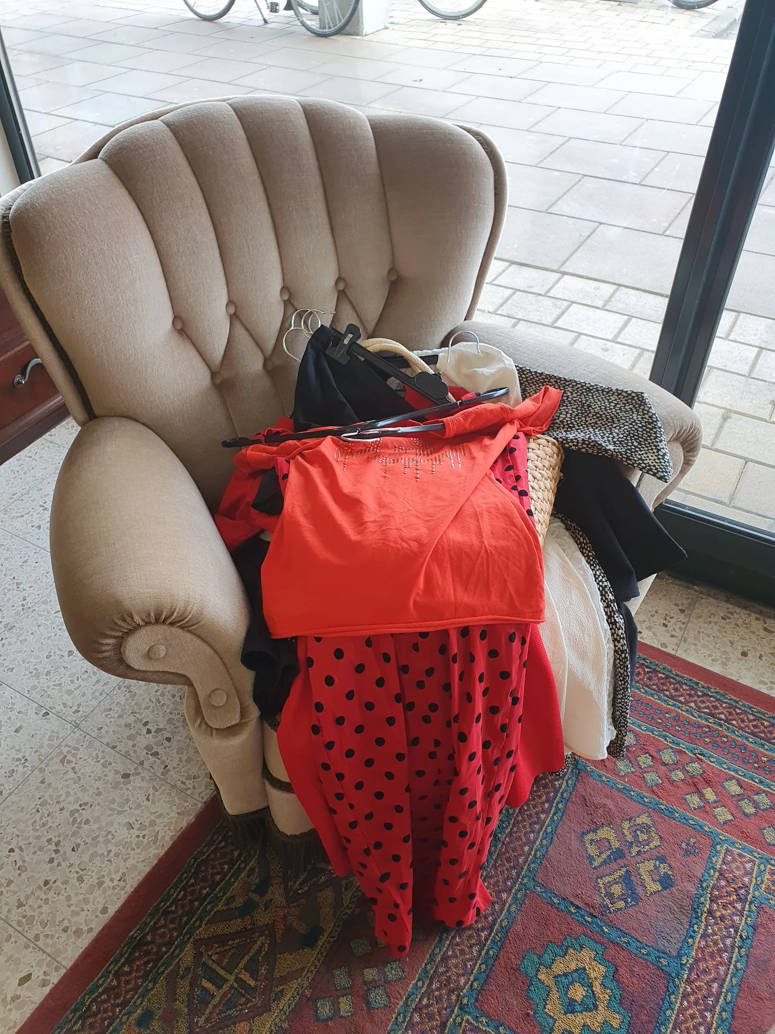 Beige fauteuil met stapel kleding en accessoires erop, waaronder rode en zwarte items