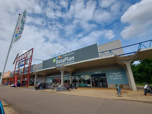 Gevel van kringloopwinkel RataPlan met groene belettering, ingang met ramen en speeltoestellen ernaast