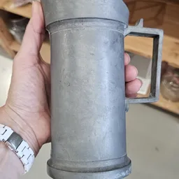 Close-up van een metalen kan of beker met rechthoekig handvat, gehouden in iemands hand