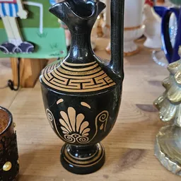 Zwarte Grieks-imitatie kan met goudkleurige decoratie en henkel op houten tafel
