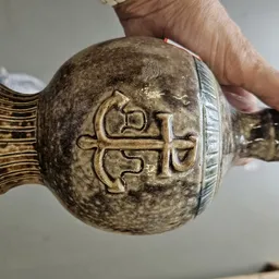 Close-up van een decoratief steengoedvat met gegraveerde kruis en geometrische patronen, gehouden in een hand