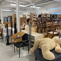 Uitgestalde meubels en huisraad in kringloopwinkel, waaronder stoelen, tafels en textiel