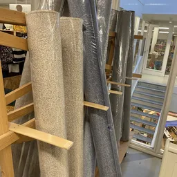 Uitgestalde tapijtrollen in verschillende kleuren op houten rekken in de winkel