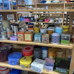 Diverse gebruikte blikken, dozen en containers met bloemen- en decoratiefmotieven op een houten plank in de winkel