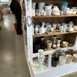 Houten stellingen met uitgestalde witte en grijze keramische vazen, schalen en decoratieve voorwerpen
