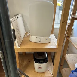 Houten tafel met tweedehands huishoudapparatuur: een magnetron, een whiteboard en een broodmachine