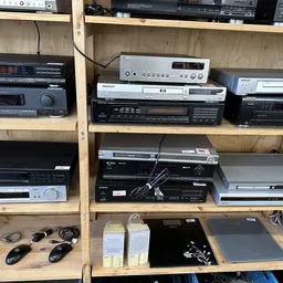Houten stellingen vol met tweedehands elektronische apparaten zoals dvd-spelers, versterkers en receivers