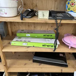 Houten stellingkast met diverse tweedehandsartikelen waaronder Athena DVD-spelers, een roze bord en huishoudelijke spullen