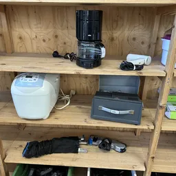 Houten stellingkast met huishoudelijke apparaten en elektronica zoals koffiemachine, broodrooster en andere gebruikte spullen
