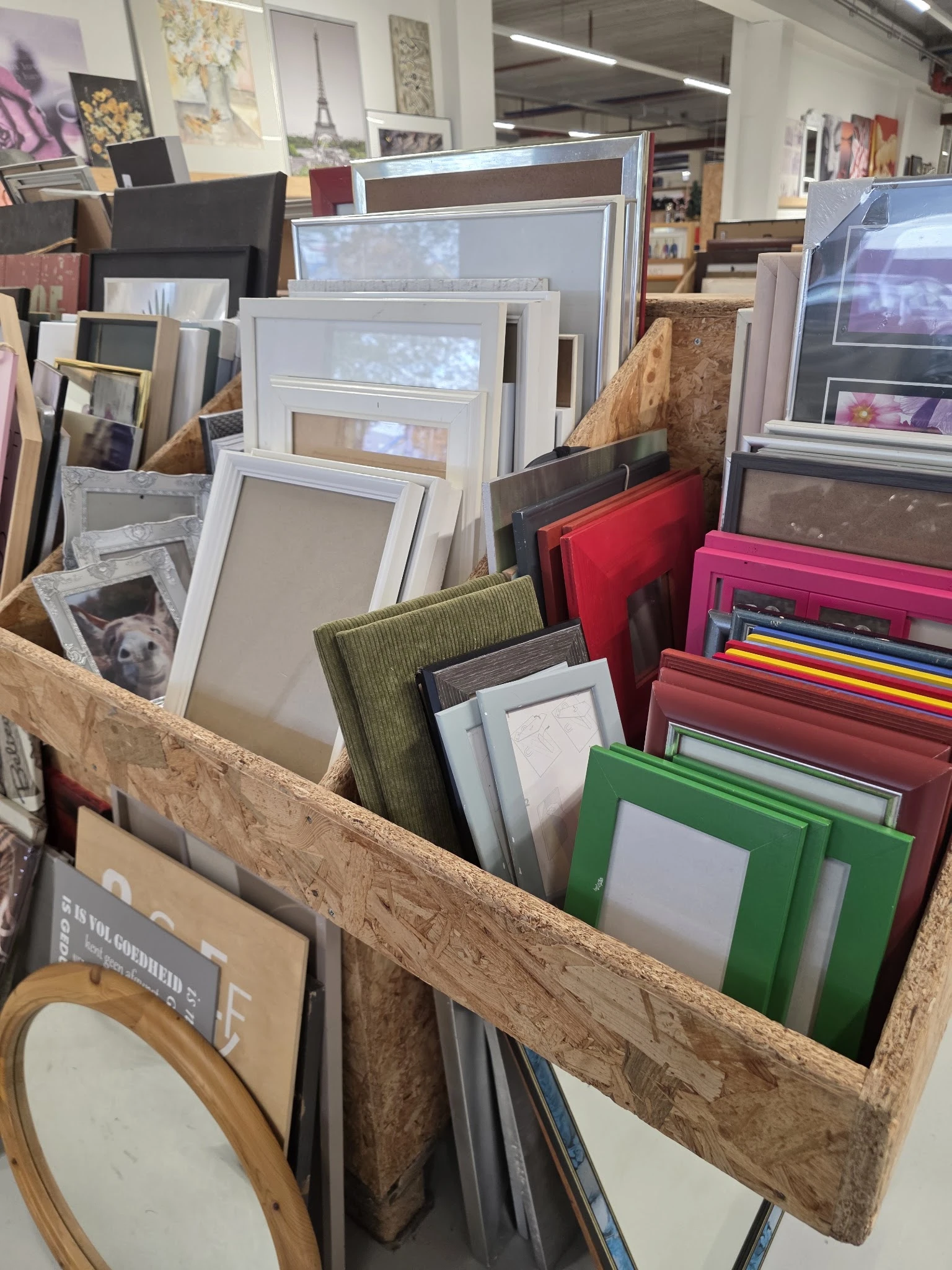 Houten kist met diverse fotolijsten in verschillende kleuren en maten, waaronder wit, groen, rood en roze.