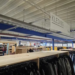 Winkelvloer met kledingrekken, stellingen en houten toonbank onder industrieel plafond met blauwe balken