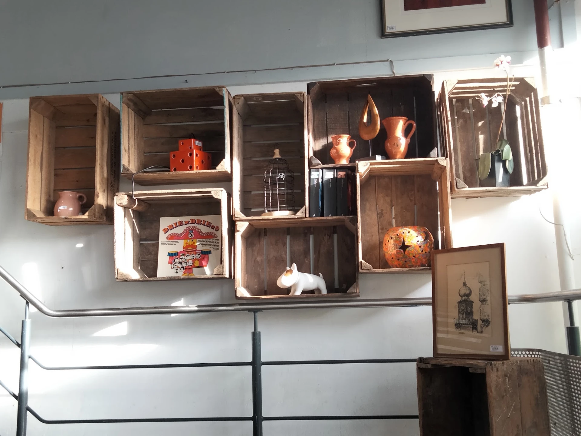 Houten kisten en kratten aan muur met decoratieve items zoals koperen kannen, servies en huishoudspullen uitgestald