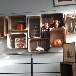 Houten kisten en kratten aan muur met decoratieve items zoals koperen kannen, servies en huishoudspullen uitgestald
