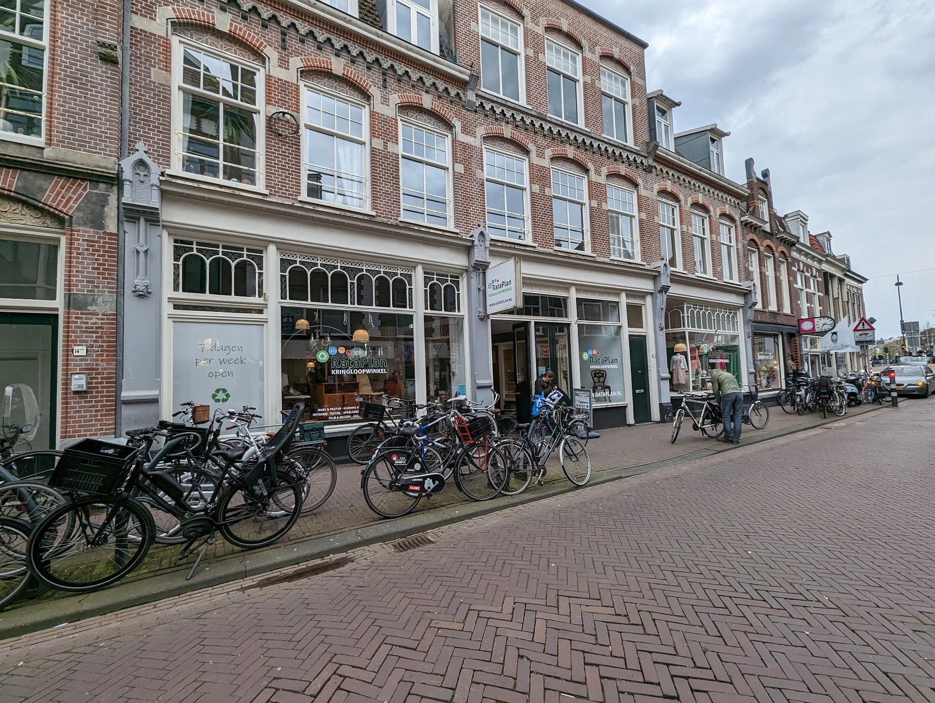 Straatgevel van kringloopwinkel met bakstenen voorgevel, uitgestalde fietsen op het trottoir en winkelramen
