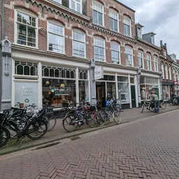 Straatgevel van kringloopwinkel met bakstenen voorgevel, uitgestalde fietsen op het trottoir en winkelramen
