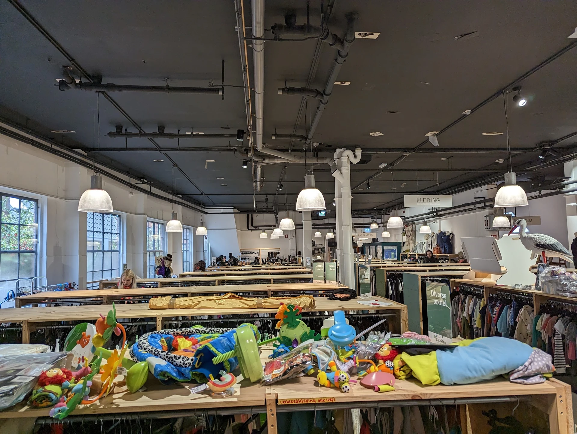 Ruim winkelinterieur met houten tafels vol kleurrijke kleding, hangende lampen en stellingen op de achtergrond