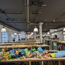 Ruim winkelinterieur met houten tafels vol kleurrijke kleding, hangende lampen en stellingen op de achtergrond