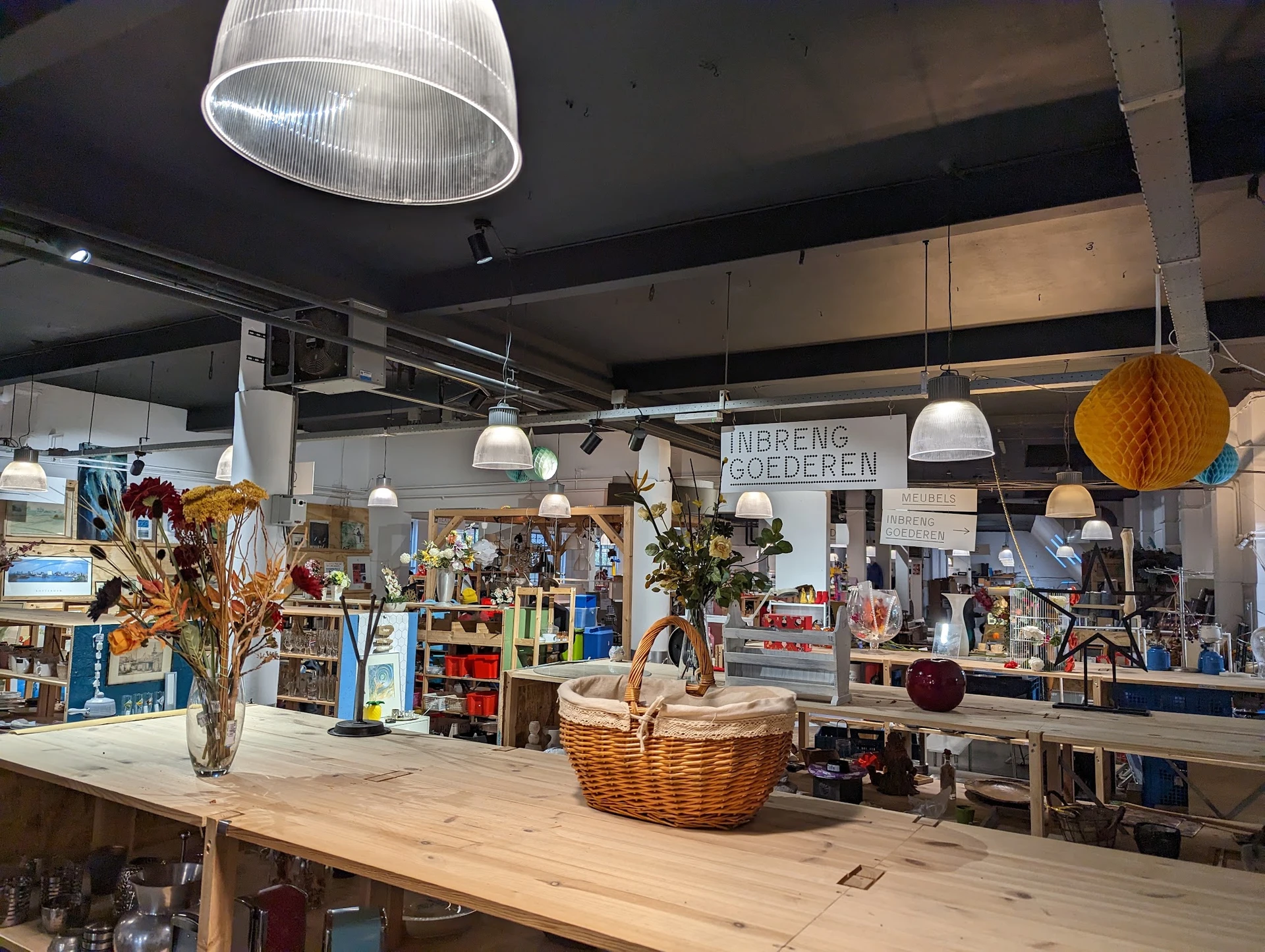 Ruime winkelruimte met houten toonbank, hangende lampen, planken met diverse artikelen en decoratieve items
