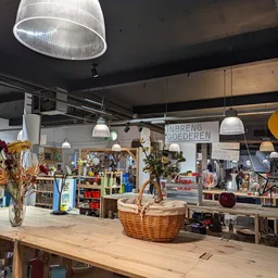 Ruime winkelruimte met houten toonbank, hangende lampen, planken met diverse artikelen en decoratieve items