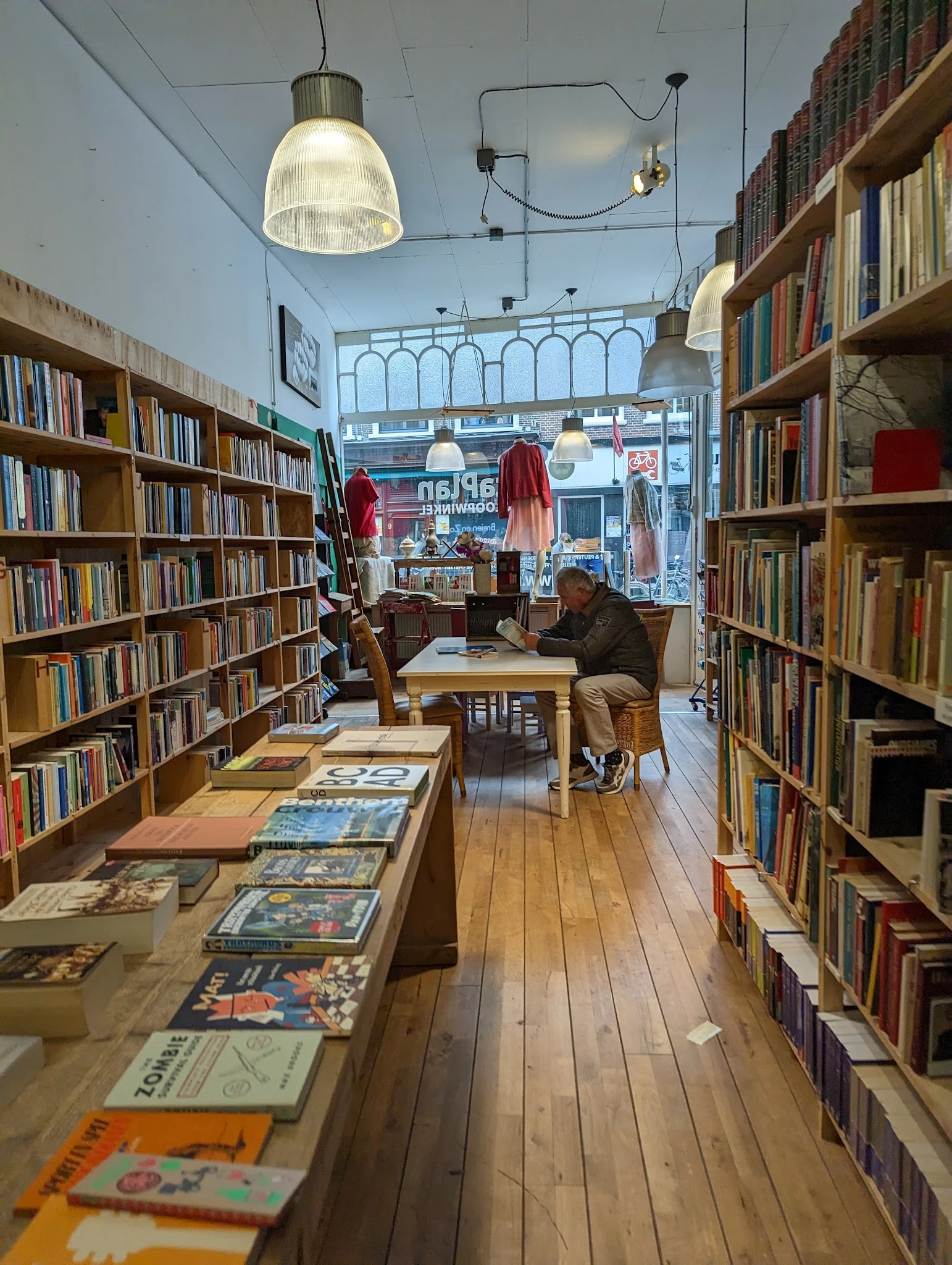 Winkelvloer met boekenrekken aan beide zijden, tafels met boeken en uitgaven, en bezoekers in de winkel