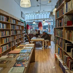 Winkelvloer met boekenrekken aan beide zijden, tafels met boeken en uitgaven, en bezoekers in de winkel