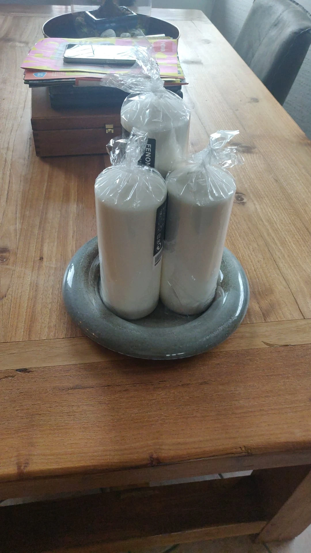 Twee witte flessen in plastic verpakking in een grijze ronde houder op houten vloer