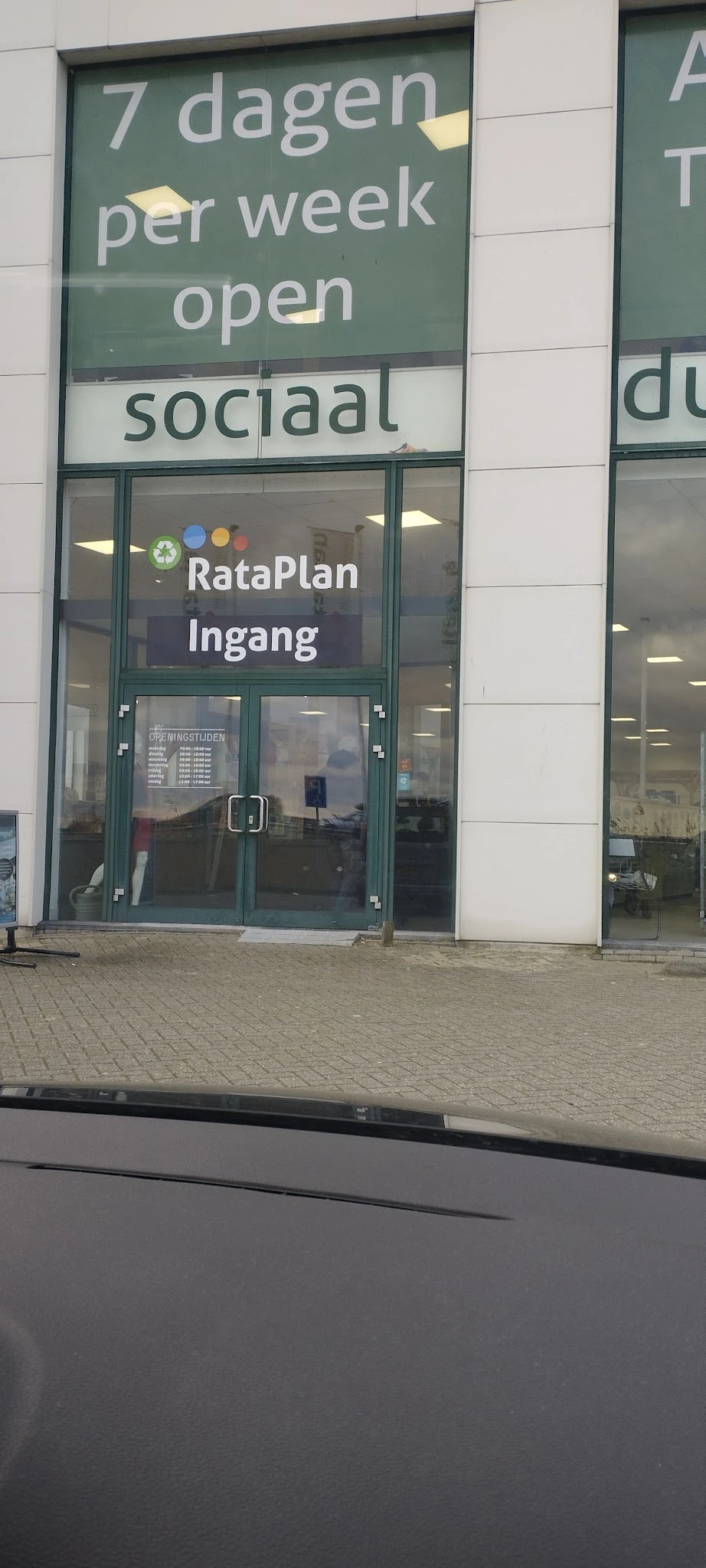 Groene glazen voordeur met 'RataPlan Ingang' opschrift en openingstijden zichtbaar