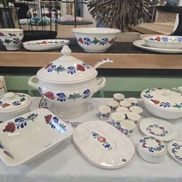 Uitstalling van wit serviesgoed met blauwe en rode bloemenpatronen: schalen, borden, tureen en kopjes