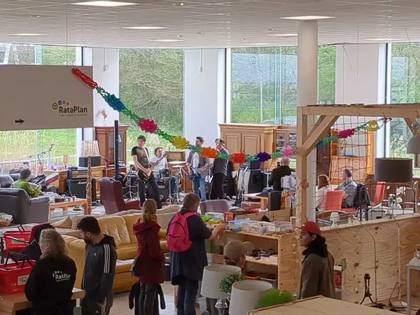 Interieur van kringloopwinkel met houten constructies, banken, veel bezoekers en grote ramen met uitzicht op groen