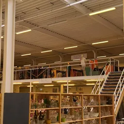 Bovenaanzicht van kringloopwinkel met twee verdiepingen, stellingen met kleding en diverse spullen, trapopgang zichtbaar