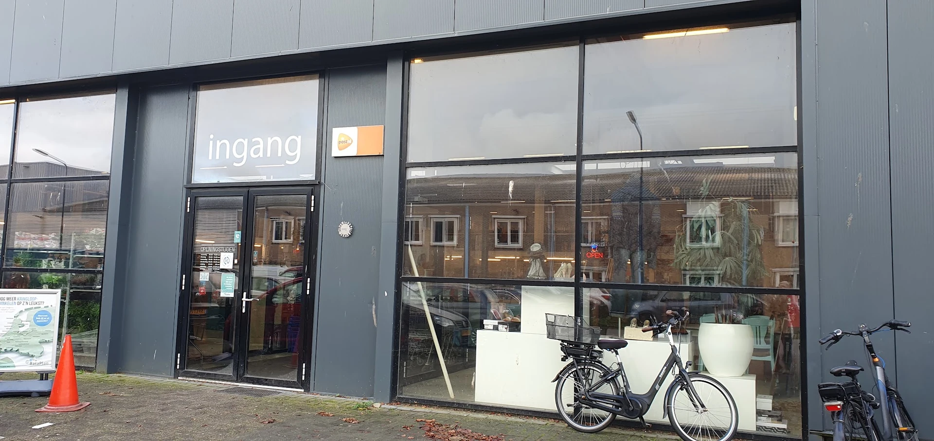 Gevel van kringloopwinkel RataPlan met grote ramen, ingangsdeuren en een fiets op het terras