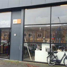 Gevel van kringloopwinkel RataPlan met grote ramen, ingangsdeuren en een fiets op het terras