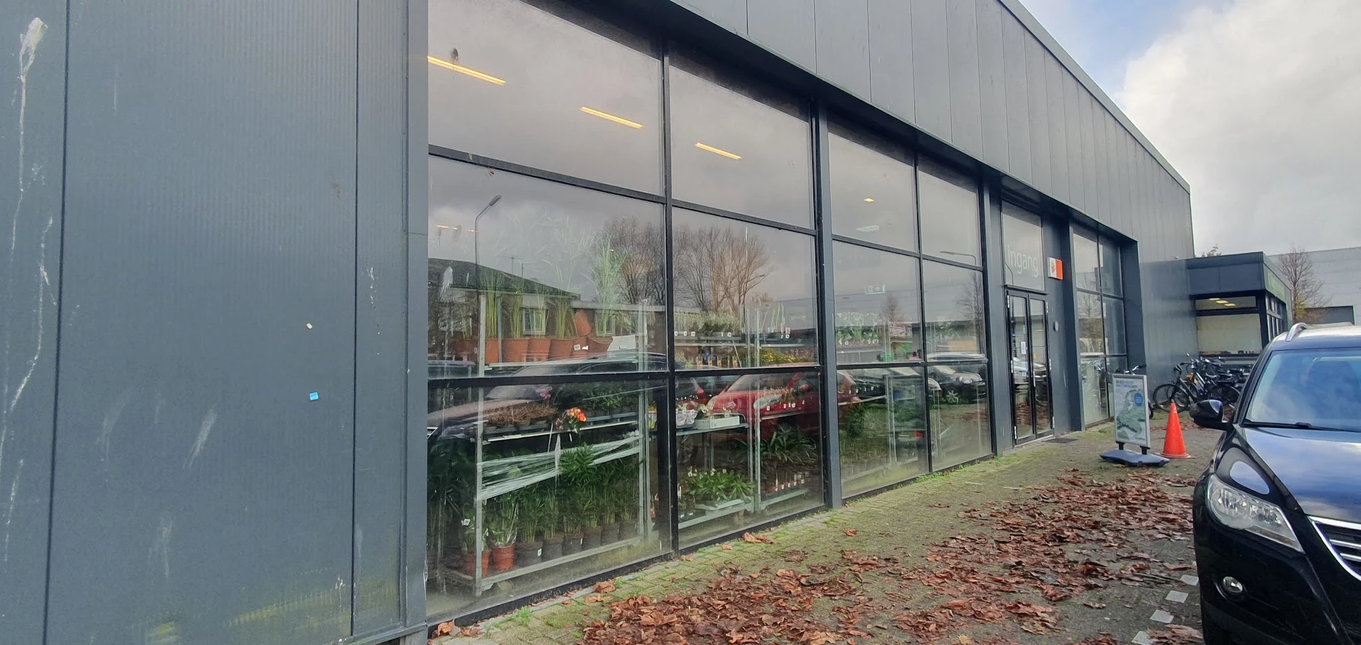 Moderne gevel van kringloopwinkel met grote raampartijen en zicht op plantjes en spullen binnen
