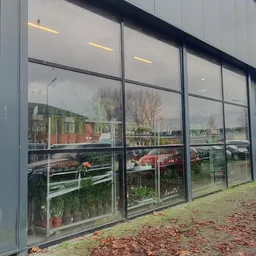 Moderne gevel van kringloopwinkel met grote raampartijen en zicht op plantjes en spullen binnen