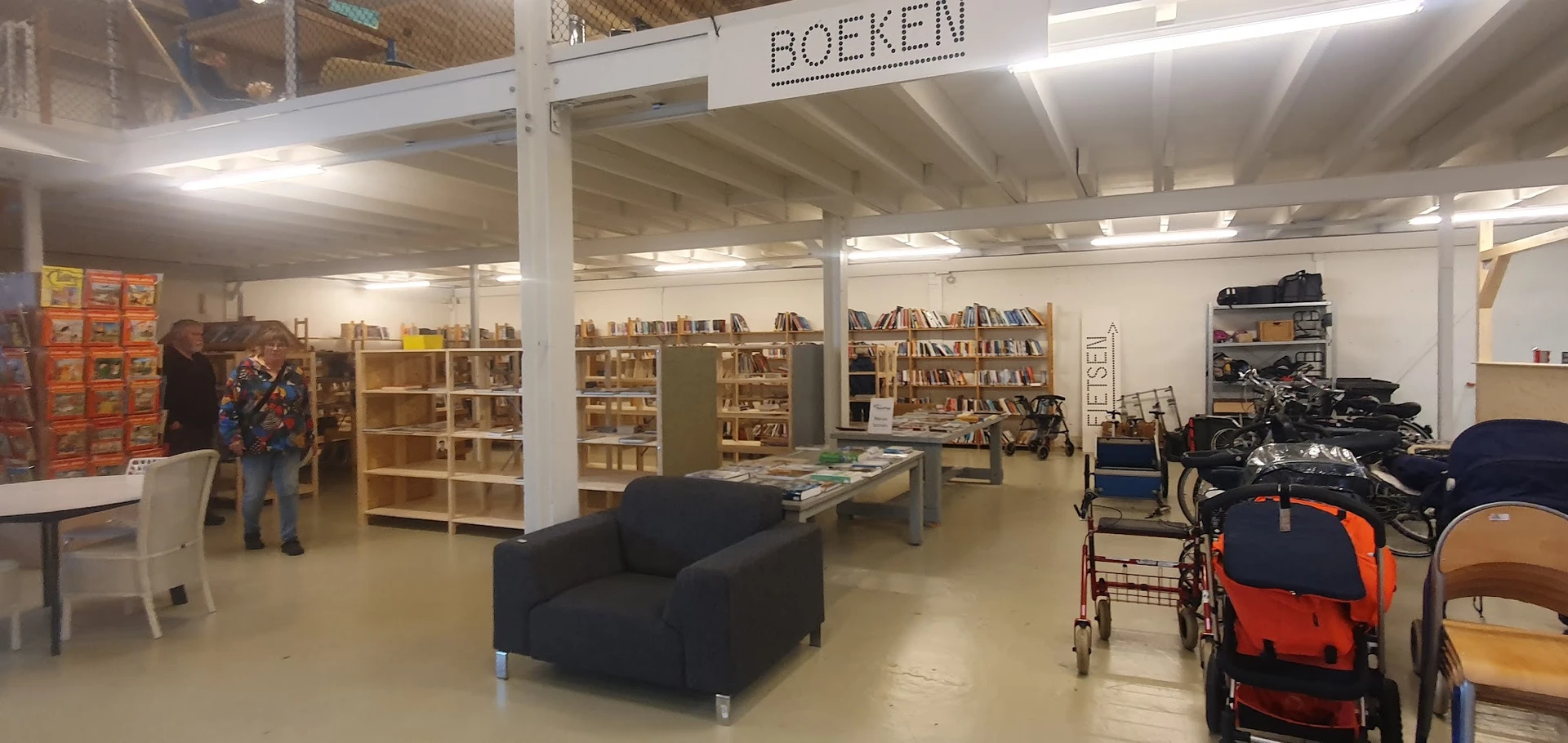 Winkelvloer van kringloopwinkel met boekenkasten, stellingen, zwarte fauteuil en diverse tweedehands artikelen