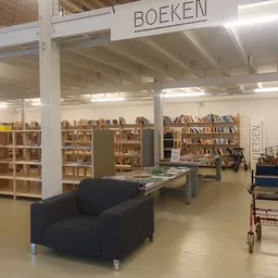 Winkelvloer van kringloopwinkel met boekenkasten, stellingen, zwarte fauteuil en diverse tweedehands artikelen