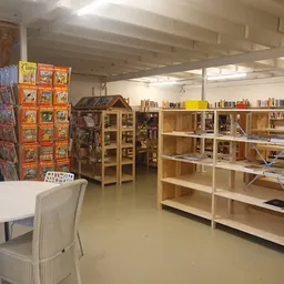 Winkelinterieur met houten stellingen vol boeken, displaykasten, een wit tafeltje met stoel op de voorgrond en een kaartenrek