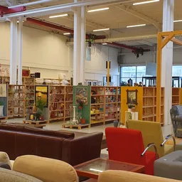 Ruim winkelinterieur met boekenrekken, zitmeubels en verschillende bruine, rode en gele kasten en stellingen