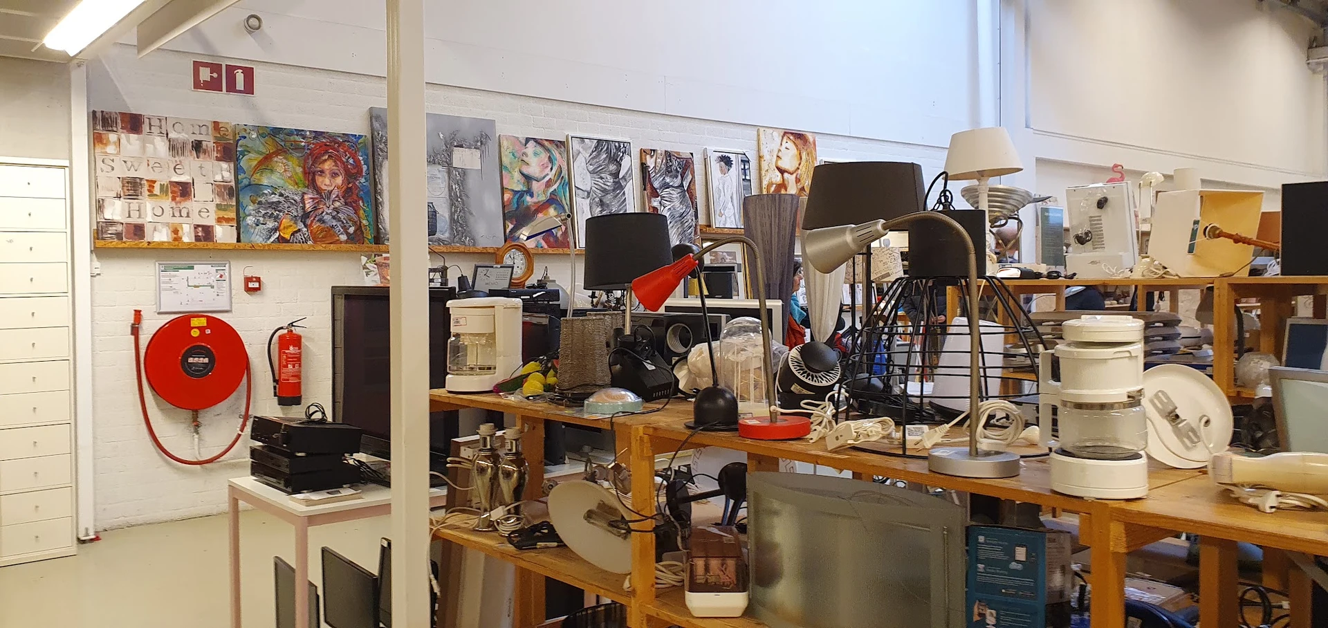 Rommelige winkelhoek met diverse gebruikte spullen, lampen, boeken en huishoudelijke artikelen op houten tafels en stellingen