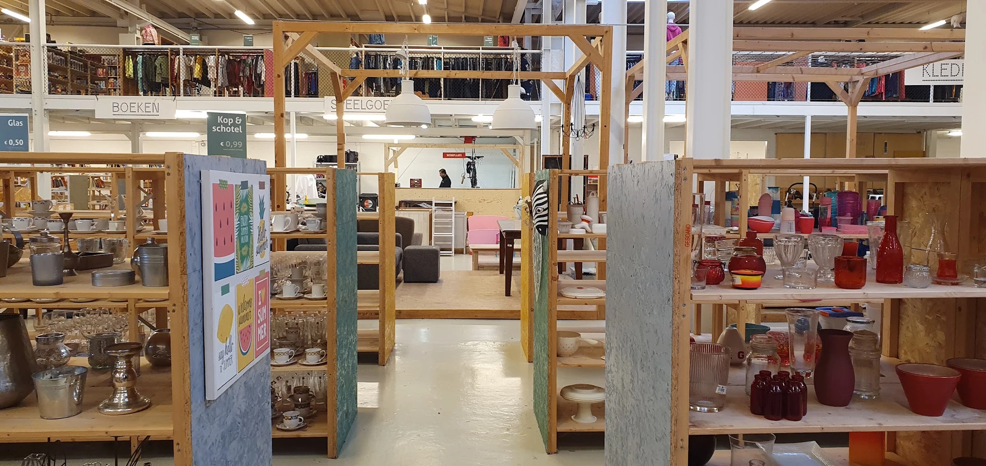 Winkelvloer met houten stellingen en vakken vol tweedehands spullen en kleding