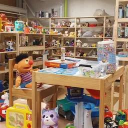 Houten werktafel met speelgoed en craft materialen, achter stellingen vol speelgoed en verzamelobjecten