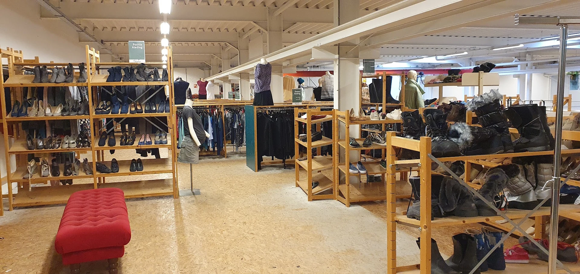 Winkelvloer met houten stellingen vol kleding, schoenen en accessoires onder LED-verlichting
