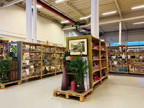 Ruim interieur van kringloopwinkel met houten stellingen vol spullen, planten en decoratie