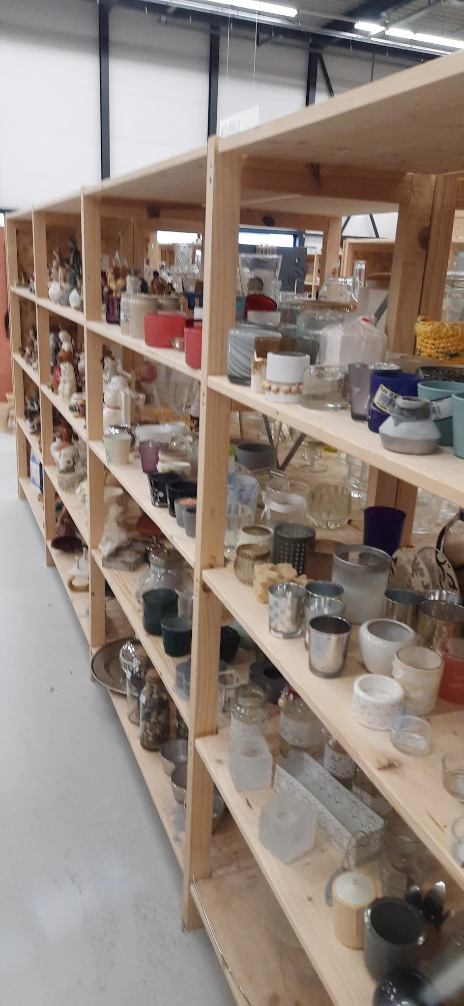 Houten stellingen met diverse huishoudelijke spullen zoals glazen, kaarsen, schalen en keramiek.