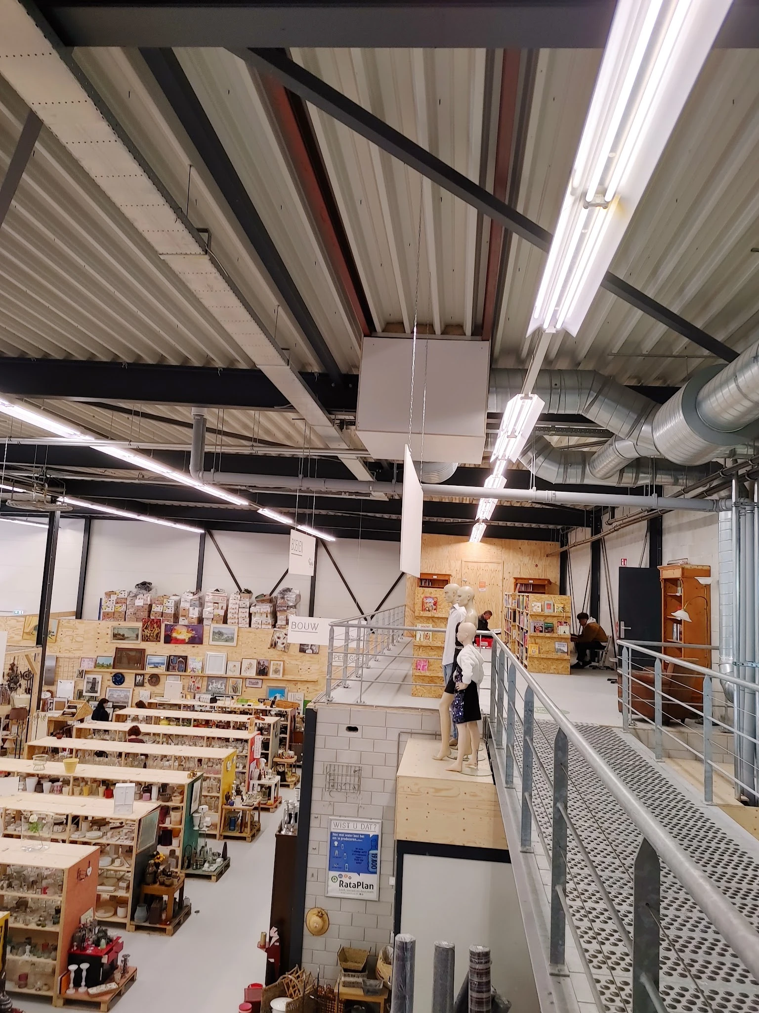 Ruim magazijn met stellingen vol kartonnen dozen en houten kasten, fluorescerende verlichting en industrieel plafond