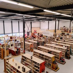 Overzicht van de kringloopwinkel met lange stellingen vol spullen, diverse afdelingen en enkele bezoekers in de ruime winkelh