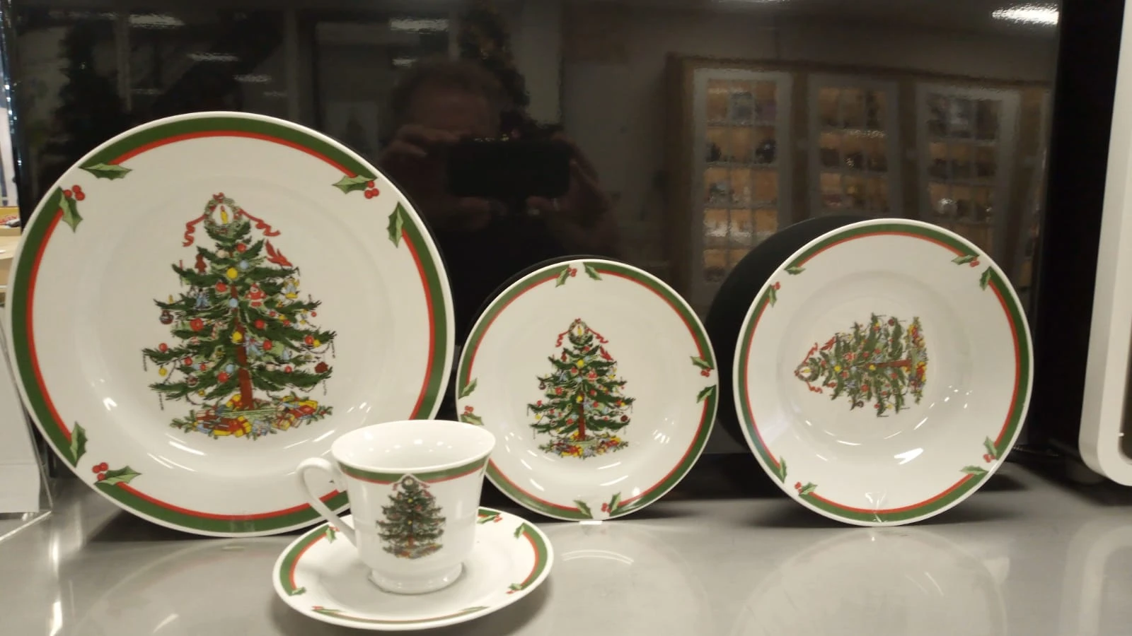 Kerstservies met kerstboomdecoratie: borden in verschillende maten, kopje en schotel met groene rand.