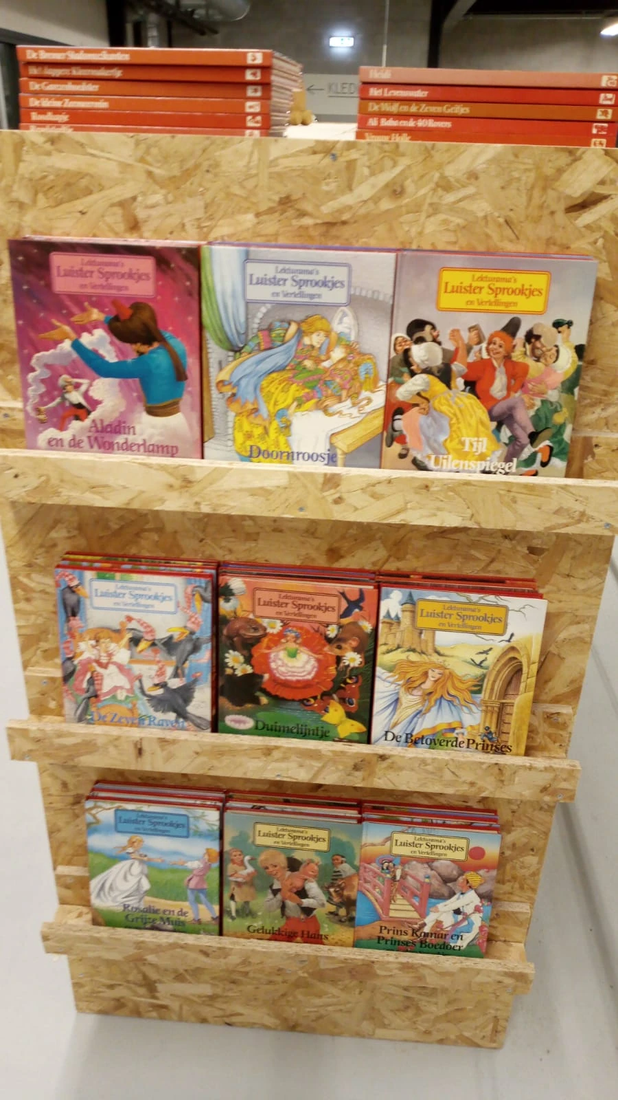 Houten stellage met kinderboeken, waaronder titels in het Nederlands zoals 'Doornroos' en 'De Betoverde Prinses'